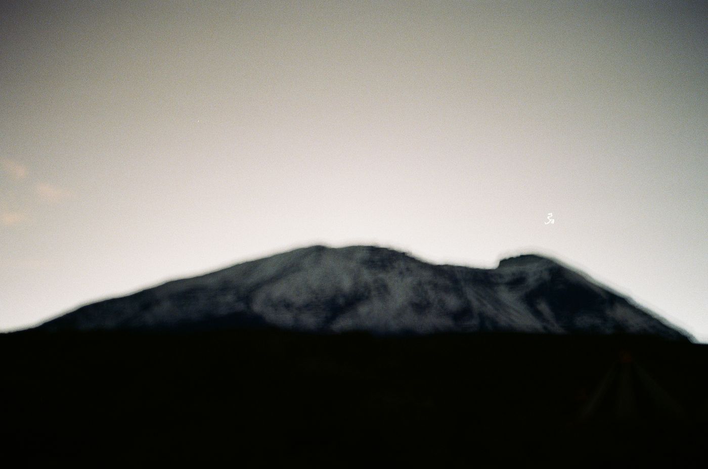A ridge line in near-silhouette against a bright blown-out sky, photographed into the light.
